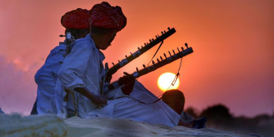 Two Folk Singers Playing Their Instruments In A Beautiful Sunset Background.