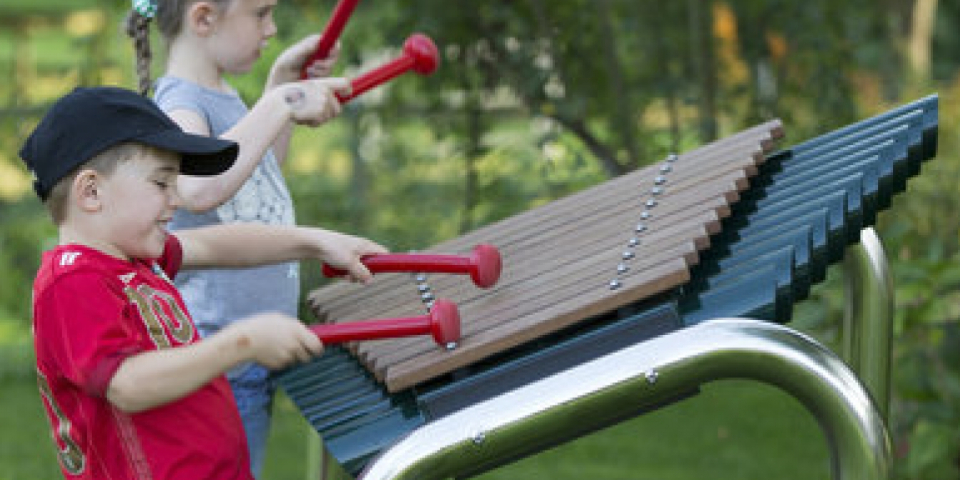 A young boy and girl playing a huge xylophone in their garden.