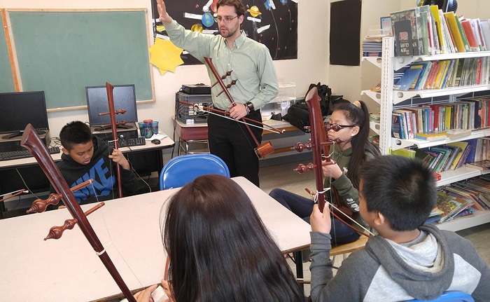 A music teacher teaches music with a musical instrument to the group of children sitting around the table with their musical instrument in their hands.